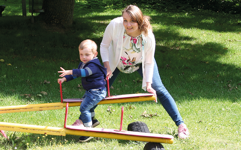 Anika ist mit Jonah auf der Spielplatzwippe und gibt ihm Schwung.